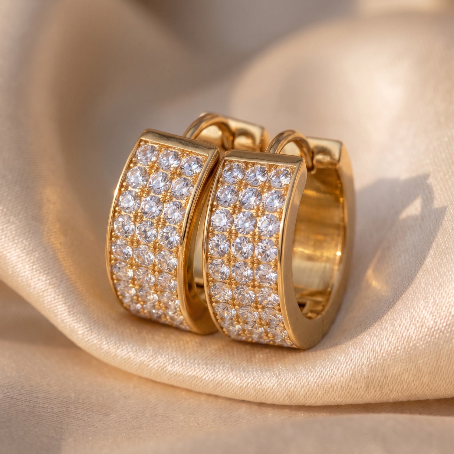 Minaz Ohrringe Soraya aus Edelstahl in Gold mit Zirkonia-Pavé, Makroaufnahme auf Champagner-Satin